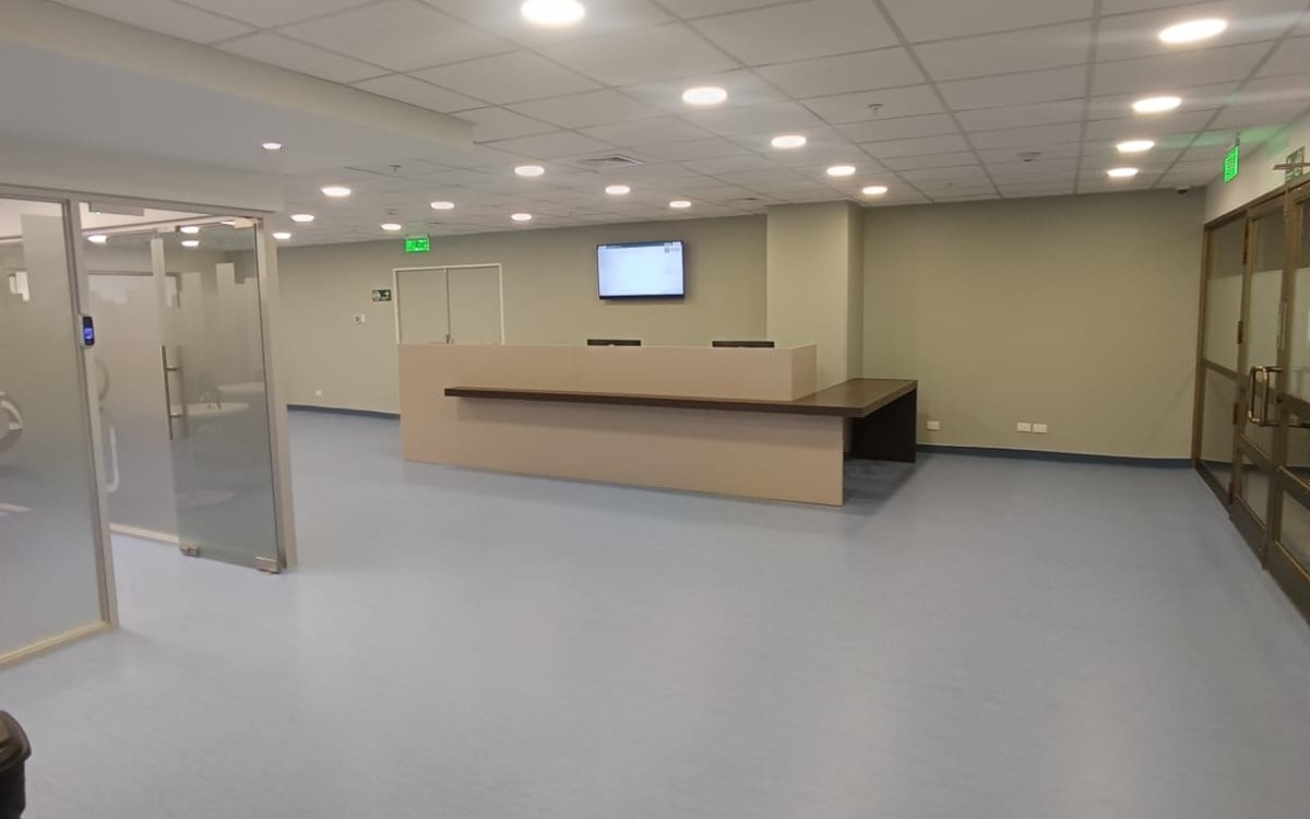 Área de recepción terminada, con mesón de atención, mamparas de vidrio y cielo americano.