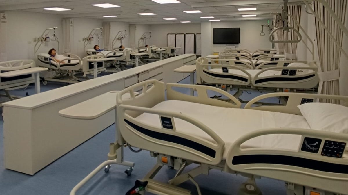 Sala de simulación clínica terminada y equipada, con camas hospitalarias, maniquíes de simulación e iluminación LED.