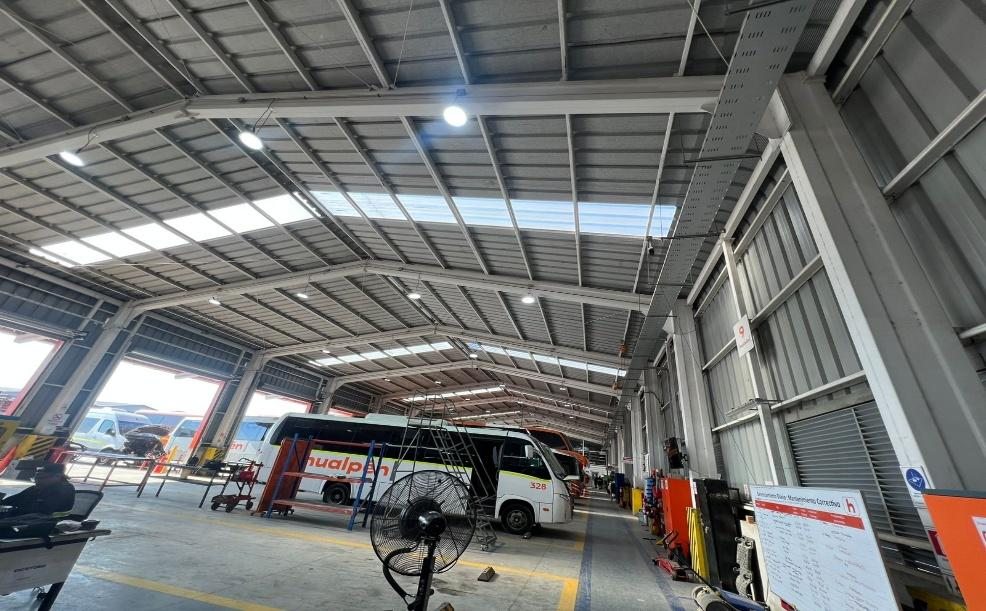 Techumbre del taller mecánico con las luminarias LED tipo UFO encendidas, y buses de la flota en mantención.